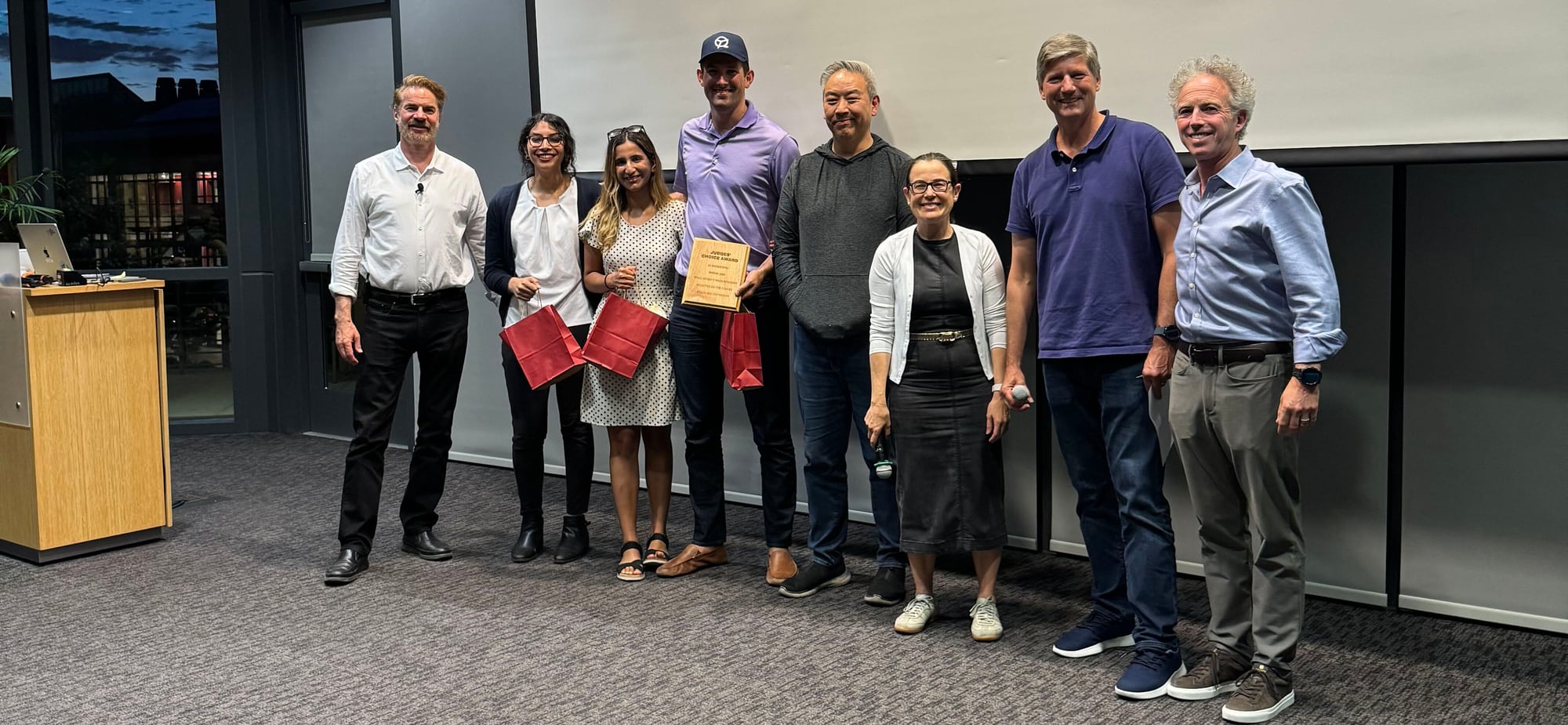 The AI Awakening project team and teaching staff on stage on the last day of class, holding the Judges' Choice Award won for QualityTime AI.